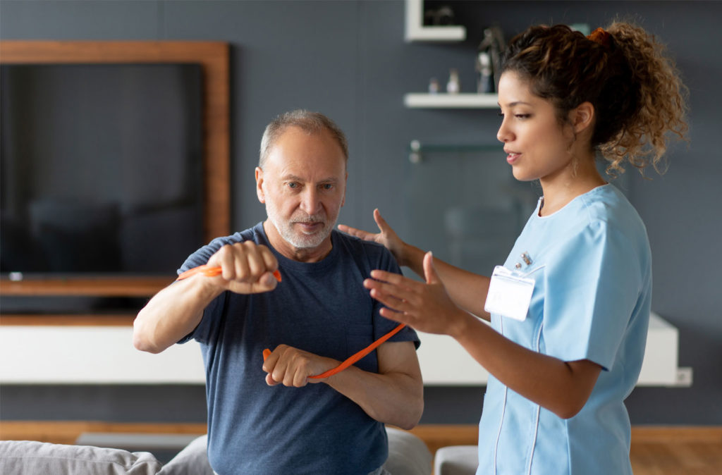 Our female healthcare professional assists an older male patient with resistance band during a therapy session.