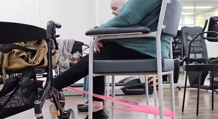 Elderly man in wheelchair doing leg exercises with resistance band for rehabilitation.