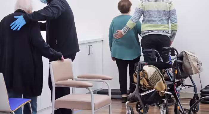 two elderly individuals being assisted by caregivers