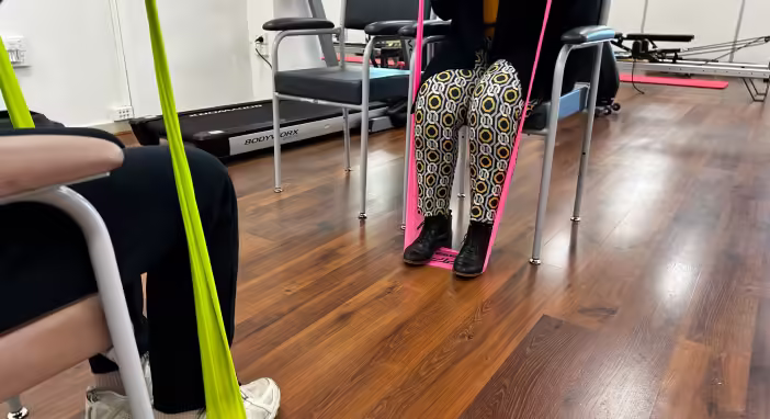 Elderly man in wheelchair doing leg exercises with resistance band for rehabilitation.