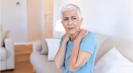 A woman experiencing shoulder pain, holding shoulder, indicating discomfort.