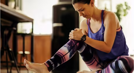 Woman experiencing knee pain during exercise or stretching, holding her knee, indicating potential injury or discomfort.