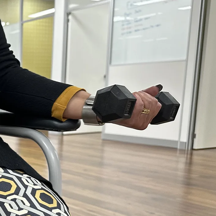 A patient performing the wrist curl exercise with dumbbell while resting their forearm on a chair armrest.