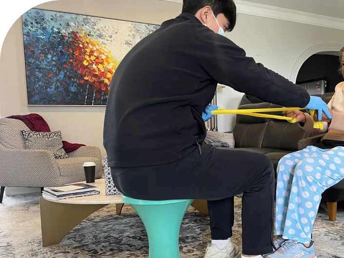 Physical therapist assisting a patient with resistance band exercises during mobile physiotherapy session in a home setting.
